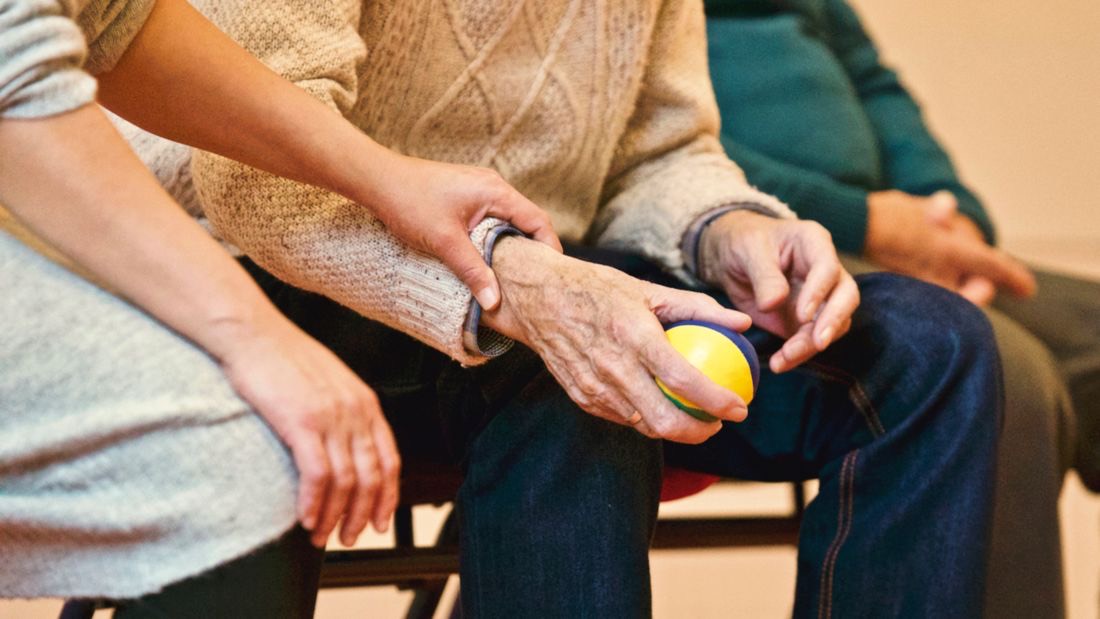 A caregiver's hand gently supporting an older man's arm
